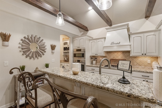 3117 S Hemlock Ct, Broken Arrow, OK 74012 - kitchen with stainless steel double oven, beam ceiling, a breakfast bar area, custom exhaust hood, and decorative backsplash