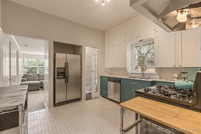 2305 E 13th St, Tulsa, OK 74104 - kitchen featuring stainless steel appliances, a sink, wall chimney exhaust hood, light countertops, and white cabinets