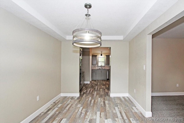 2005 Holly Rd, Claremore, OK 74017 - empty room featuring a tray ceiling, wood finished floors, a sink, and baseboards