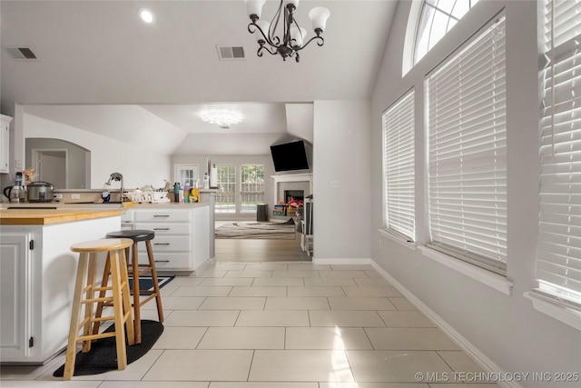 1105 N Joshua Ave, Broken Arrow, OK 74012 - kitchen with a peninsula, vaulted ceiling, a chandelier, white cabinetry, and light tile patterned floors