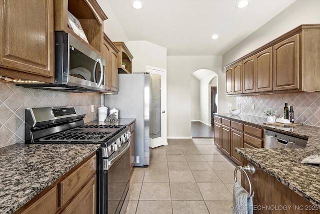 1620 E Granger St, Broken Arrow, OK 74012 - kitchen featuring appliances with stainless steel finishes, arched walkways, dark stone countertops, light tile patterned floors, and tasteful backsplash