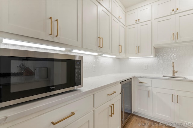 10215 E 121st Pl S, Bixby, OK 74008 - kitchen featuring stainless steel microwave, a sink, wine cooler, white cabinetry, and backsplash