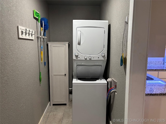 914 3rd Ave NE, Ardmore, OK 73401 - laundry area with stacked washer and clothes dryer, a textured wall, cabinet space, light tile patterned floors, and baseboards