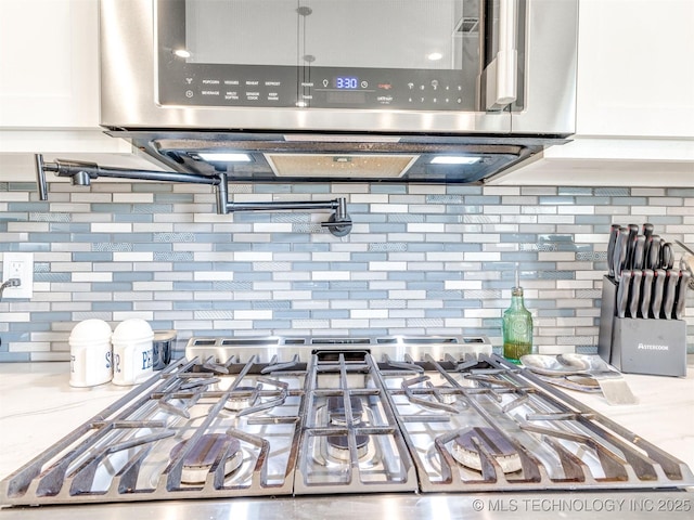 23814 E 91st St S, Broken Arrow, OK 74014 - kitchen view of pot filler, backsplash, stainless steel microwave, and white cabinets