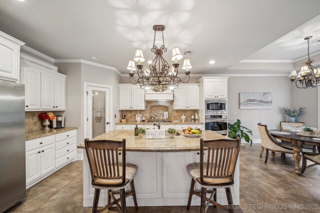 7734 S Indian Ave, Tulsa, OK 74132 - kitchen featuring appliances with stainless steel finishes, a chandelier, a kitchen bar, tasteful backsplash, and white cabinetry
