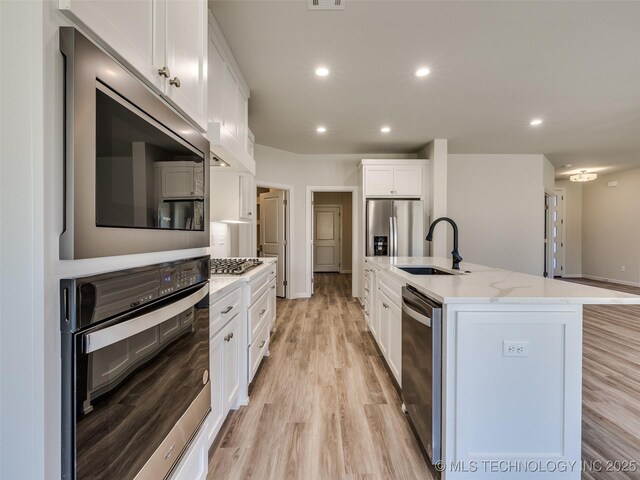 3011 S 6th Pl, Broken Arrow, OK 74012 - kitchen with appliances with stainless steel finishes, a sink, light wood-type flooring, white cabinets, and an island with sink