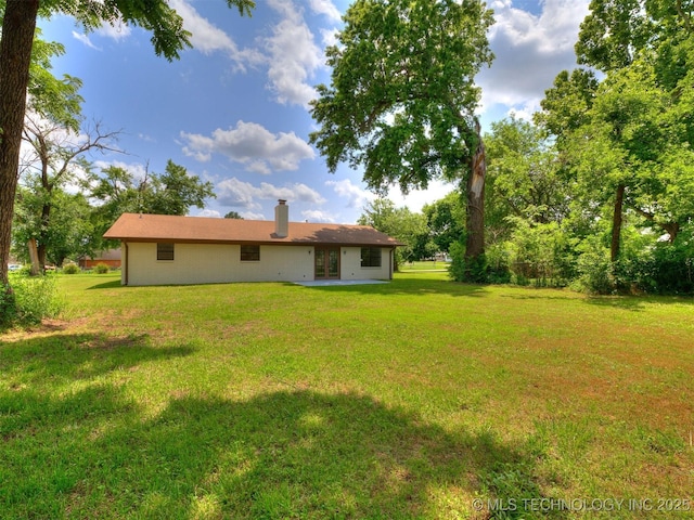 703 NE 8th St, Wagoner, OK 74467 - back of property with french doors, a lawn, a chimney, and a patio