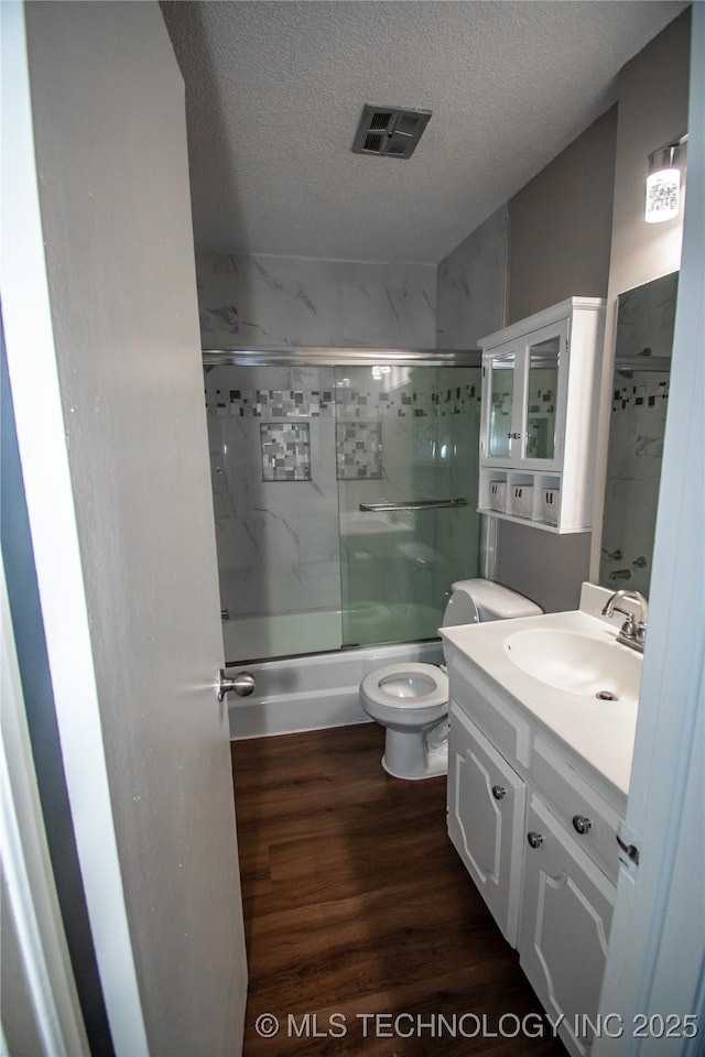 11612 E 28th St, Tulsa, OK 74129 - full bathroom featuring wood finished floors, vanity, combined bath / shower with glass door, a textured ceiling, and toilet