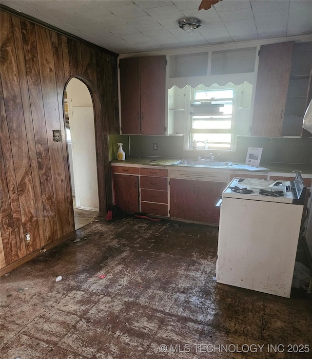 737 W Doolin Ave, Blackwell, OK 74631 - kitchen with white gas range, a sink, wooden walls, arched walkways, and light countertops