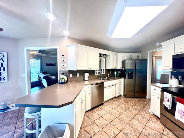 1403 NW Mimosa Cir, Stigler, OK 74462 - kitchen with stainless steel appliances, a peninsula, a kitchen bar, white cabinetry, and a sink