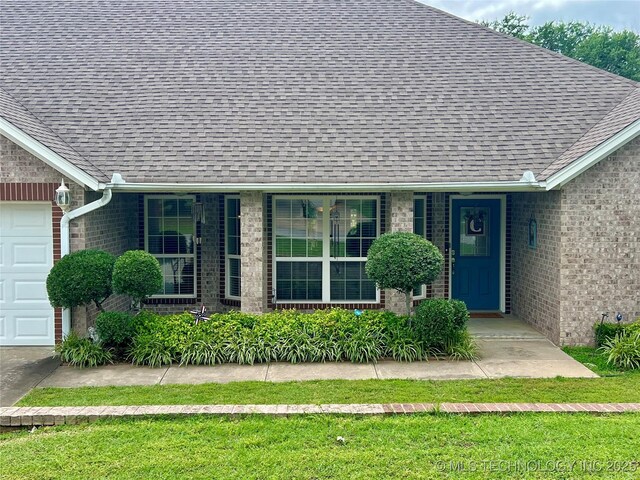 1403 NW Mimosa Cir, Stigler, OK 74462 - view of exterior entry featuring a shingled roof, brick siding, and a garage