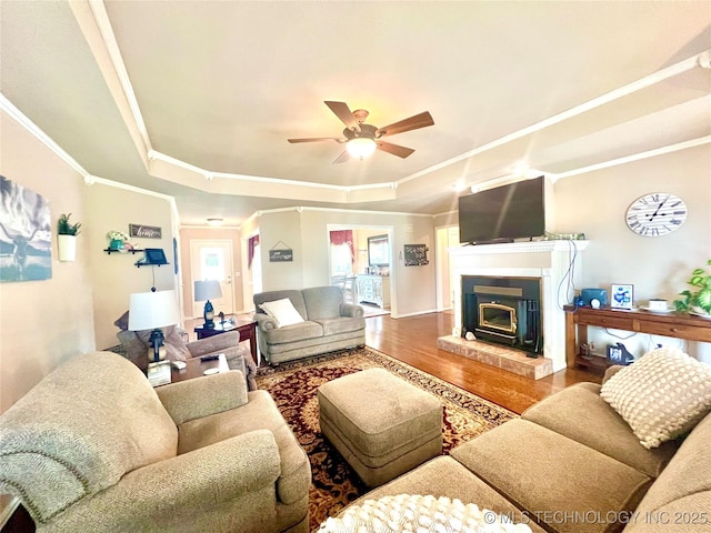 1403 NW Mimosa Cir, Stigler, OK 74462 - living room featuring a raised ceiling, wood finished floors, ornamental molding, a ceiling fan, and a glass covered fireplace
