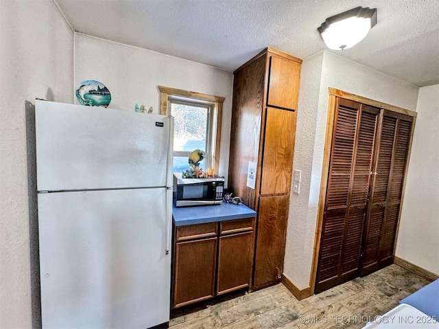 31663 S 530th Rd, Cookson, OK 74427 - kitchen featuring freestanding refrigerator, stainless steel microwave, light wood finished floors, a textured ceiling, and baseboards
