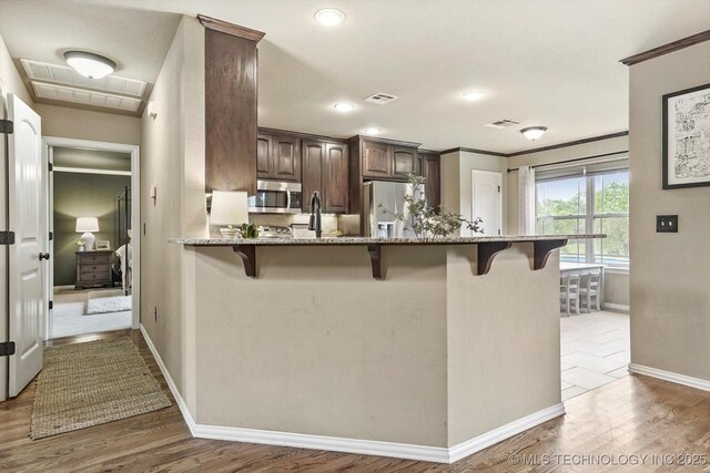 14355 N Trenton Ave, Skiatook, OK 74070 - kitchen featuring appliances with stainless steel finishes, a breakfast bar area, dark brown cabinetry, light stone counters, and ornamental molding