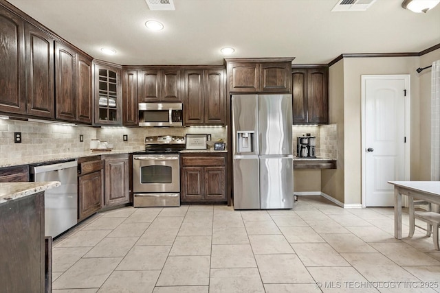 14355 N Trenton Ave, Skiatook, OK 74070 - kitchen with appliances with stainless steel finishes, decorative backsplash, dark brown cabinetry, light stone countertops, and glass insert cabinets