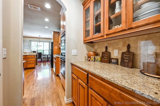 11715 S 93rd E Ave, Bixby, OK 74008 - kitchen featuring brown cabinetry, arched walkways, light stone countertops, recessed lighting, and light wood-type flooring