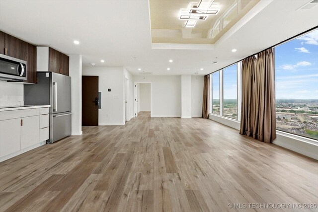 5810 E Skelly Dr Unit 303, Tulsa, OK 74135 - unfurnished living room featuring light wood-style flooring, recessed lighting, and a raised ceiling