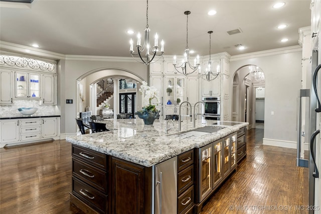 5879 N Eagle Summit Rd, Owasso, OK 74055 - kitchen with arched walkways, a chandelier, white cabinetry, a large island with sink, and tasteful backsplash