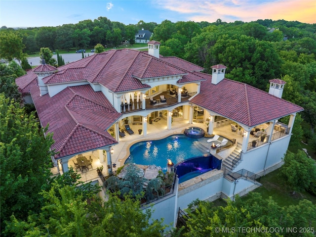 5879 N Eagle Summit Rd, Owasso, OK 74055 - back of property at dusk with a balcony, a tile roof, a chimney, a pool with connected hot tub, and a patio