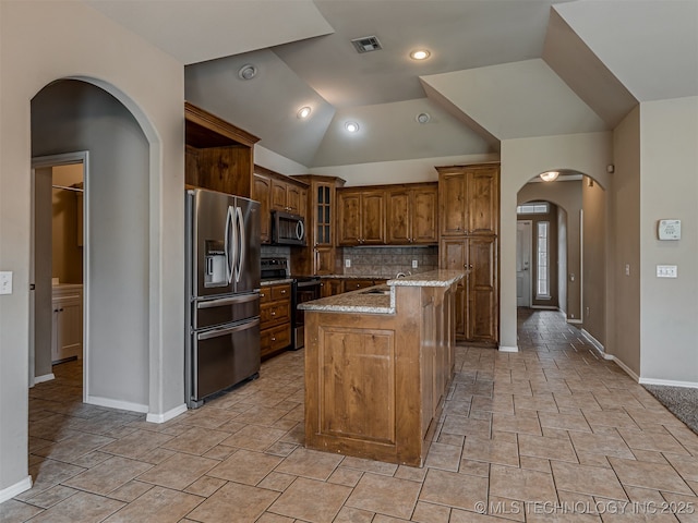 4610 E 142nd St S, Bixby, OK 74008 - kitchen featuring appliances with stainless steel finishes, arched walkways, decorative backsplash, a kitchen island with sink, and light stone counters