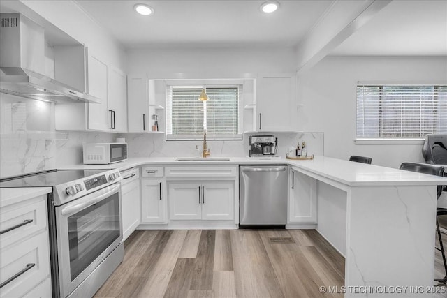 1008 E 54th St S, Tulsa, OK 74105 - kitchen with stainless steel appliances, wall chimney range hood, a sink, a peninsula, and white cabinetry
