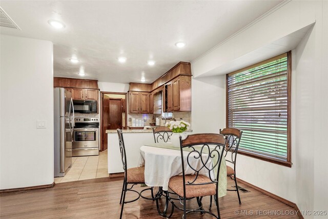 911 S Boyd Pl, Sapulpa, OK 74066 - kitchen featuring appliances with stainless steel finishes, brown cabinetry, a peninsula, tasteful backsplash, and baseboards