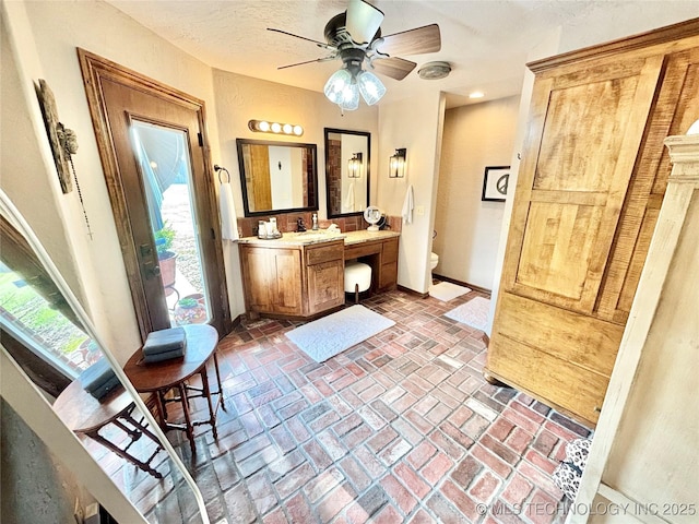 2102 N Peaceful Ln, Stigler, OK 74462 - bathroom featuring baseboards, vanity, toilet, brick floors, and ceiling fan