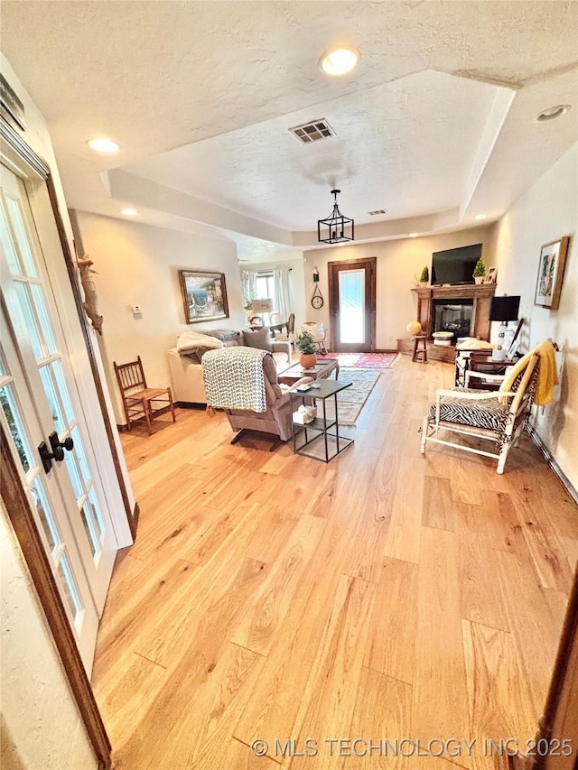 2102 N Peaceful Ln, Stigler, OK 74462 - bedroom featuring light wood-style flooring, a tray ceiling, a textured ceiling, a glass covered fireplace, and french doors