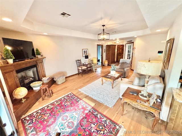 2102 N Peaceful Ln, Stigler, OK 74462 - living room featuring a tray ceiling, a fireplace with raised hearth, wood finished floors, recessed lighting, and baseboards