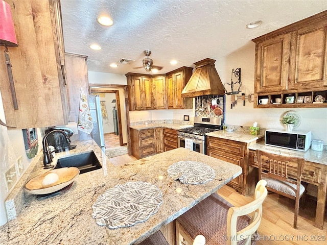 2102 N Peaceful Ln, Stigler, OK 74462 - kitchen featuring stainless steel gas stove, black microwave, a sink, brown cabinets, and light wood-type flooring