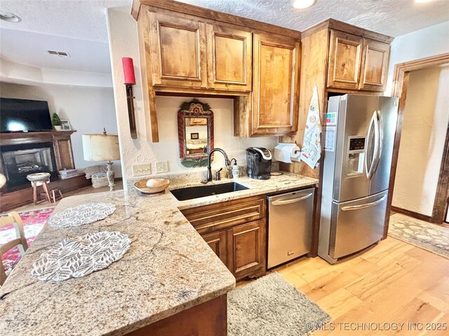 2102 N Peaceful Ln, Stigler, OK 74462 - kitchen with stainless steel appliances, a sink, light wood finished floors, a textured ceiling, and brown cabinets