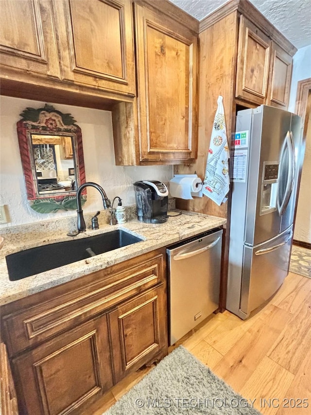 2102 N Peaceful Ln, Stigler, OK 74462 - kitchen with appliances with stainless steel finishes, a sink, light wood-style flooring, and brown cabinets