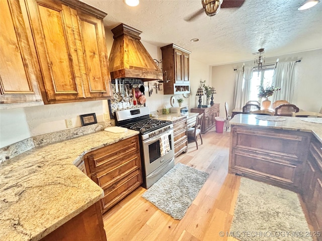2102 N Peaceful Ln, Stigler, OK 74462 - kitchen with stainless steel gas range, light wood finished floors, premium range hood, ceiling fan, and a textured ceiling