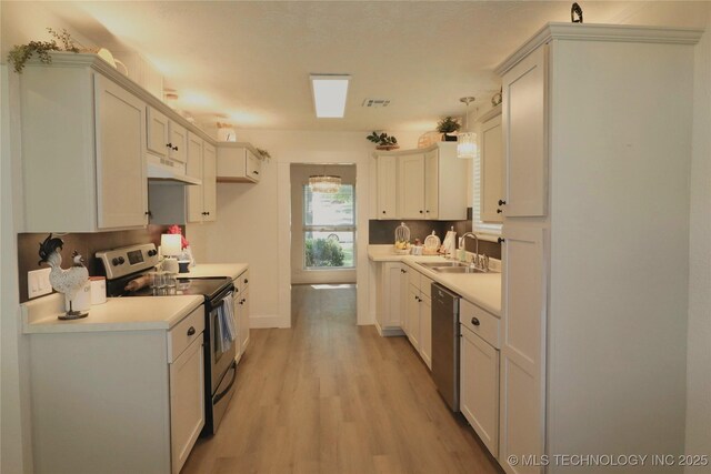 1100 Guinn Ln, Bartlesville, OK 74006 - kitchen with appliances with stainless steel finishes, under cabinet range hood, a sink, light wood-style floors, and light countertops