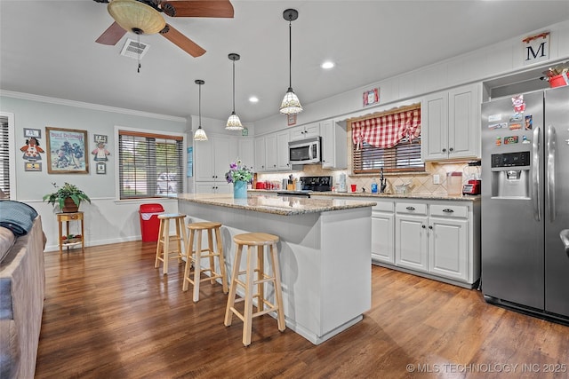 1307 Chickasaw Rd, Calera, OK 74730 - kitchen featuring appliances with stainless steel finishes, crown molding, white cabinetry, a breakfast bar, and wood finished floors