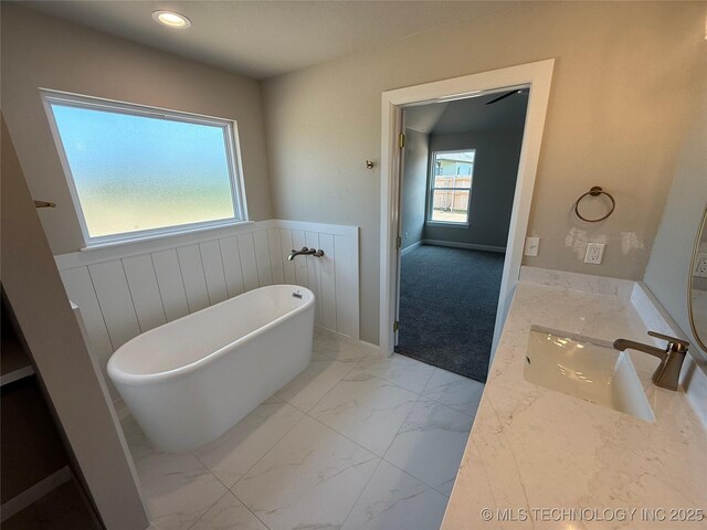 22832 E 106th Pl S, Broken Arrow, OK 74014 - bathroom featuring marble look tiles, a soaking tub, vanity, wainscoting, and recessed lighting
