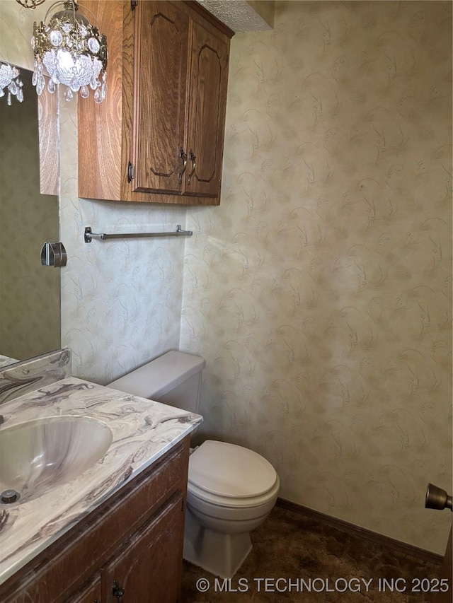 1339 E 9th St, Cushing, OK 74023 - bathroom featuring toilet, vanity, wallpapered walls, a chandelier, and baseboards