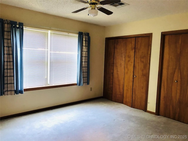 3814 E Dripping Springs Rd, Cushing, OK 74023 - unfurnished bedroom with carpet floors, multiple windows, two closets, baseboards, and a textured ceiling