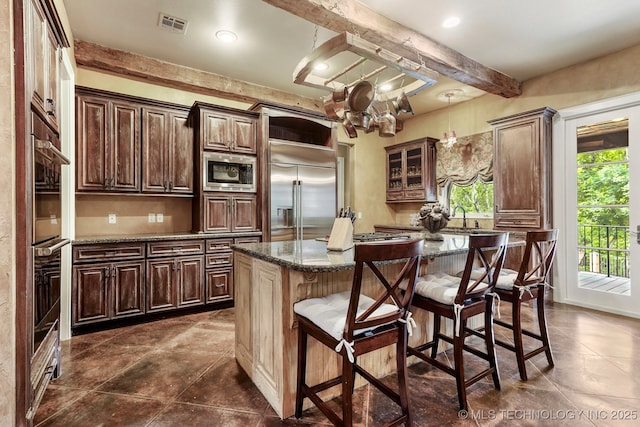 10144 N Dover Pl, Owasso, OK 74055 - kitchen featuring built in appliances, a breakfast bar, beamed ceiling, dark stone counters, and a kitchen island