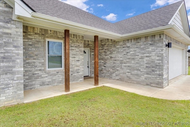 153 Founders Ln, Durant, OK 74701 - view of exterior entry with a shingled roof, brick siding, a lawn, and a garage