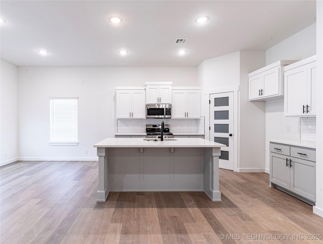 1404 E 149th Pl S, Glenpool, OK 74033 - kitchen with appliances with stainless steel finishes, an island with sink, decorative backsplash, light countertops, and light wood-style floors