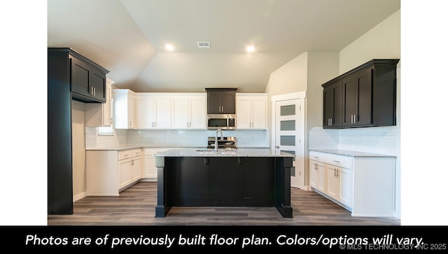 1411 E 149th Pl S, Glenpool, OK 74033 - kitchen with stainless steel microwave, vaulted ceiling, light stone counters, wood finished floors, and a center island with sink