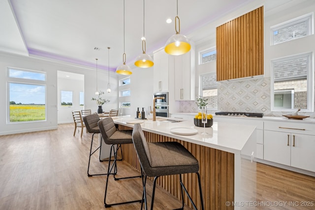 2357 E 134th Cir, Bixby, OK 74008 - kitchen featuring appliances with stainless steel finishes, tasteful backsplash, a breakfast bar, a kitchen island with sink, and white cabinets