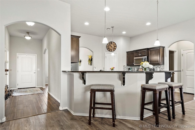 2023 E 133rd St S, Bixby, OK 74008 - kitchen featuring stainless steel microwave, a kitchen breakfast bar, dark brown cabinetry, dark wood finished floors, and arched walkways