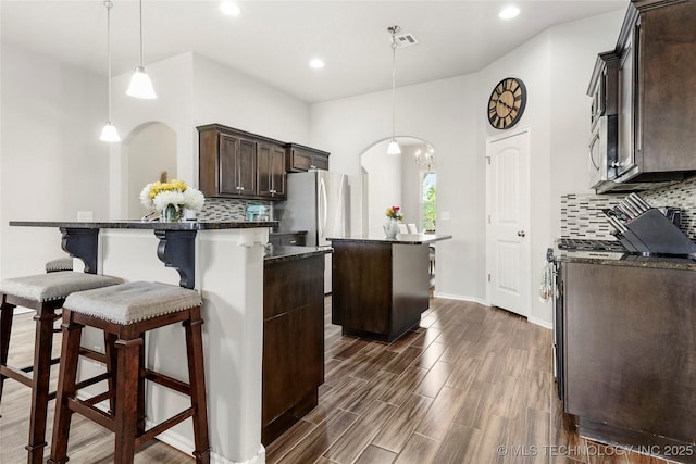 2023 E 133rd St S, Bixby, OK 74008 - kitchen featuring stainless steel appliances, a center island, dark brown cabinetry, decorative backsplash, and arched walkways