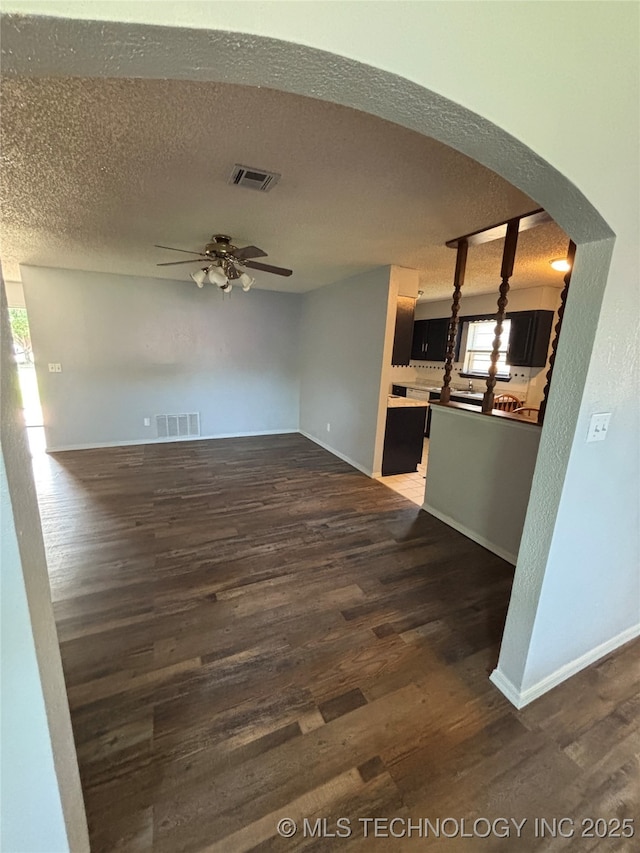 1310 S 38th St, Muskogee, OK 74401 - unfurnished living room featuring a ceiling fan, dark wood-style floors, arched walkways, baseboards, and a textured ceiling