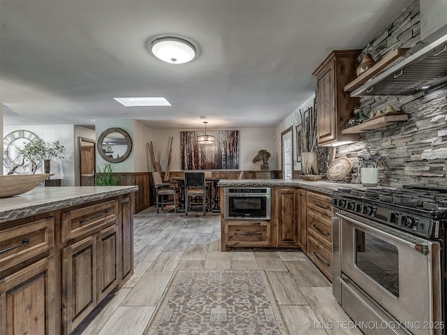 32188 E 738th Rd, Wagoner, OK 74467 - kitchen featuring stainless steel gas range, a wainscoted wall, a peninsula, dark stone countertops, and wood finish floors