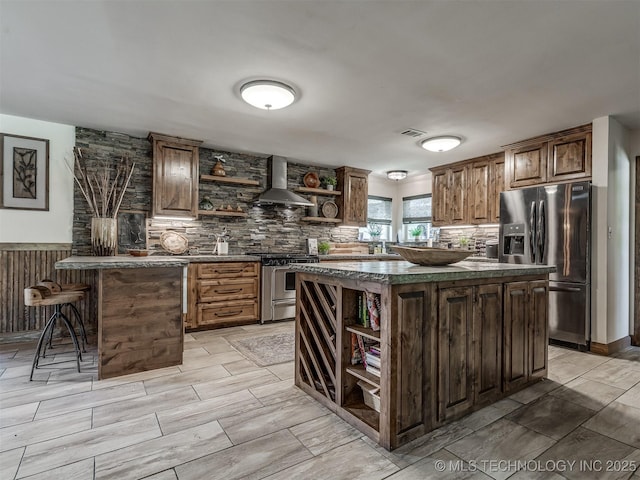 32188 E 738th Rd, Wagoner, OK 74467 - kitchen with open shelves, appliances with stainless steel finishes, wall chimney exhaust hood, dark countertops, and a kitchen bar