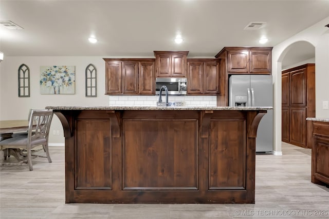 12441 S 209th W Ave, Sapulpa, OK 74066 - kitchen with stainless steel appliances, tasteful backsplash, arched walkways, a kitchen island with sink, and light stone counters