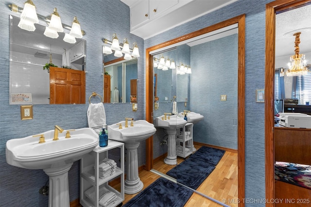722 E 18th St, Ada, OK 74820 - bathroom featuring wood finished floors, a chandelier, two sinks, and baseboards